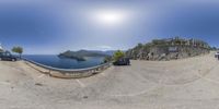 a 360 - view photo showing car driving along a curve by a beach and hill