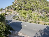 the paved highway is narrow and winding near the sea side with large rocks on both sides