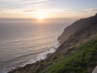 a person sitting on a hill overlooking the ocean and ocean waves at sunset time looking out over the ocean