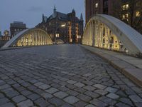 a bridge over a cobblestone street in a city at dusk with many buildings