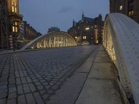 a bridge over a cobblestone street in a city at dusk with many buildings