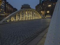 a bridge over a cobblestone street in a city at dusk with many buildings