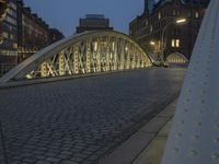 a bridge over a cobblestone street in a city at dusk with many buildings