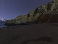 the sky is clear and the stars glow behind the cliffs and beach below it that looks like the moon rises