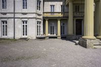 a statue is sitting on the gravel outside a building with columns and steps leading into the courtyard