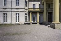 a statue is sitting on the gravel outside a building with columns and steps leading into the courtyard