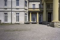 a statue is sitting on the gravel outside a building with columns and steps leading into the courtyard