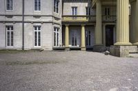 a statue is sitting on the gravel outside a building with columns and steps leading into the courtyard