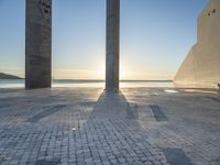 a statue is standing in a large empty building next to the ocean at sunset and some people are sitting on benches in front