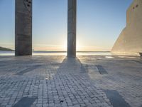 a statue is standing in a large empty building next to the ocean at sunset and some people are sitting on benches in front