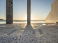 a statue is standing in a large empty building next to the ocean at sunset and some people are sitting on benches in front