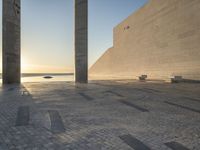 a statue is standing in a large empty building next to the ocean at sunset and some people are sitting on benches in front