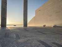 a statue is standing in a large empty building next to the ocean at sunset and some people are sitting on benches in front