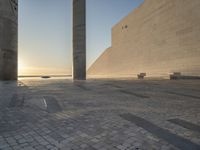 a statue is standing in a large empty building next to the ocean at sunset and some people are sitting on benches in front