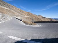 a curved road going up to a mountain peak side with a sky background and a few shadows