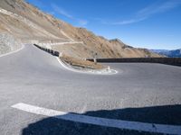 a curved road going up to a mountain peak side with a sky background and a few shadows