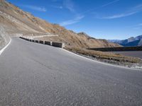 a curved road going up to a mountain peak side with a sky background and a few shadows