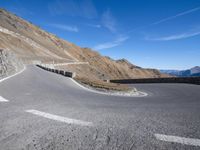 a curved road going up to a mountain peak side with a sky background and a few shadows