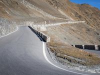 a curved road going up to a mountain peak side with a sky background and a few shadows