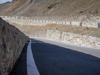 road next to cliff with large stone wall near road side area and sign on right