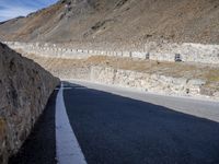 road next to cliff with large stone wall near road side area and sign on right