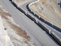 a lone motor bike is traveling down the road near a curve and stones wall beside the winding roads