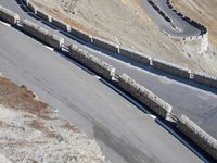 a lone motor bike is traveling down the road near a curve and stones wall beside the winding roads