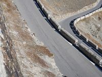 a lone motor bike is traveling down the road near a curve and stones wall beside the winding roads