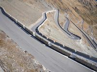 a lone motor bike is traveling down the road near a curve and stones wall beside the winding roads