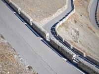 a lone motor bike is traveling down the road near a curve and stones wall beside the winding roads