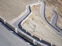 a lone motor bike is traveling down the road near a curve and stones wall beside the winding roads