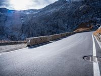 an empty road near a cliff on the mountain side with snow capped mountains in the background