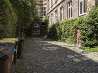 a stone alley way lined with tall buildings and garbage cans in front of the door