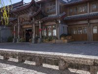 stone bench in front of a long building with many chinese decor on it, with a building behind