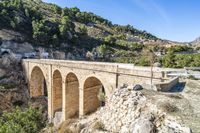 an old stone bridge with cars over it in a valley with mountain range behind the road