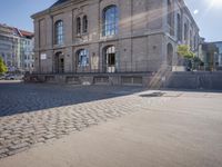 the sidewalk in front of a large stone building on a sunny day with sun shining on it