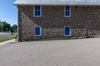 the stone building has three blue windows in the front, and the brick walkway with a fire hydrant on the back of it