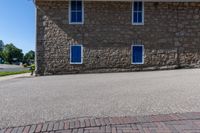 the stone building has three blue windows in the front, and the brick walkway with a fire hydrant on the back of it