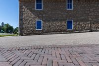 the stone building has three blue windows in the front, and the brick walkway with a fire hydrant on the back of it