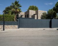 a black gate is in front of a stone building and palm trees behind it in the foreground