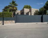 a black gate is in front of a stone building and palm trees behind it in the foreground