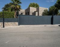 a black gate is in front of a stone building and palm trees behind it in the foreground