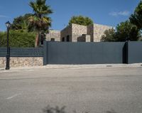 a black gate is in front of a stone building and palm trees behind it in the foreground