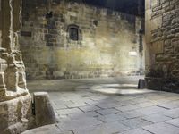 a small stone courtyard with light coming through the opening in the stone wall and through the arch at it