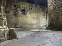 a small stone courtyard with light coming through the opening in the stone wall and through the arch at it