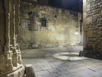 a small stone courtyard with light coming through the opening in the stone wall and through the arch at it