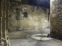 a small stone courtyard with light coming through the opening in the stone wall and through the arch at it