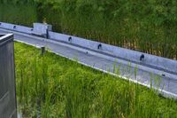 a stone drainage and a wall with three black pipeholes surrounded by green vegetation on the side of the road