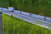 a stone drainage and a wall with three black pipeholes surrounded by green vegetation on the side of the road