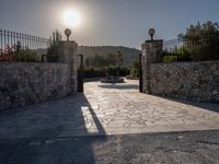 a stone fence sits near a stone building and gate in the country setting of a greek property